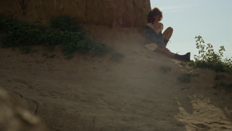 Pretty-woman-relax-leaning-sand-hill-on-empty-seashore.-Lady-shaking-curly-hair.