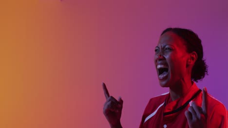 Happy-african-american-female-rugby-player-raising-hands-over-neon-pink-lighting