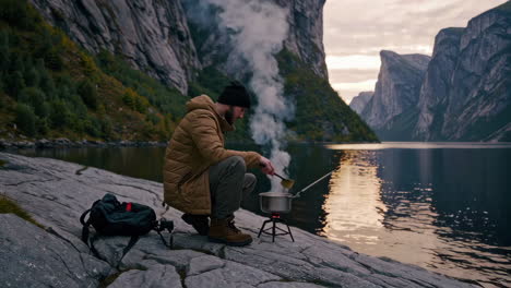 man cooking outdoors in a fjord landscape