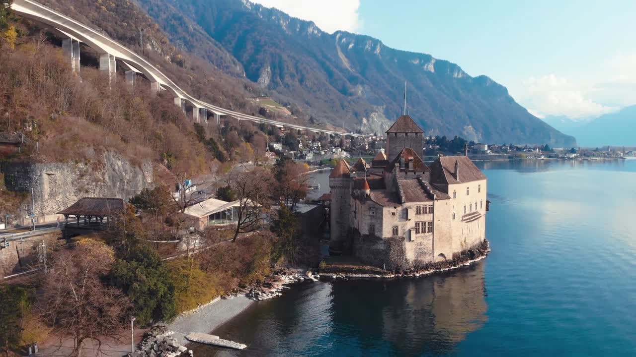 Drone captures historic building nestled between majestic mountains and serene lake, bathed in natural daylight, showcasing picturesque beauty Switzerland's alpine landscape
