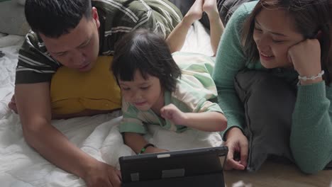 happy asian family lying prone on living room floor and watching video with tablet computer together at home