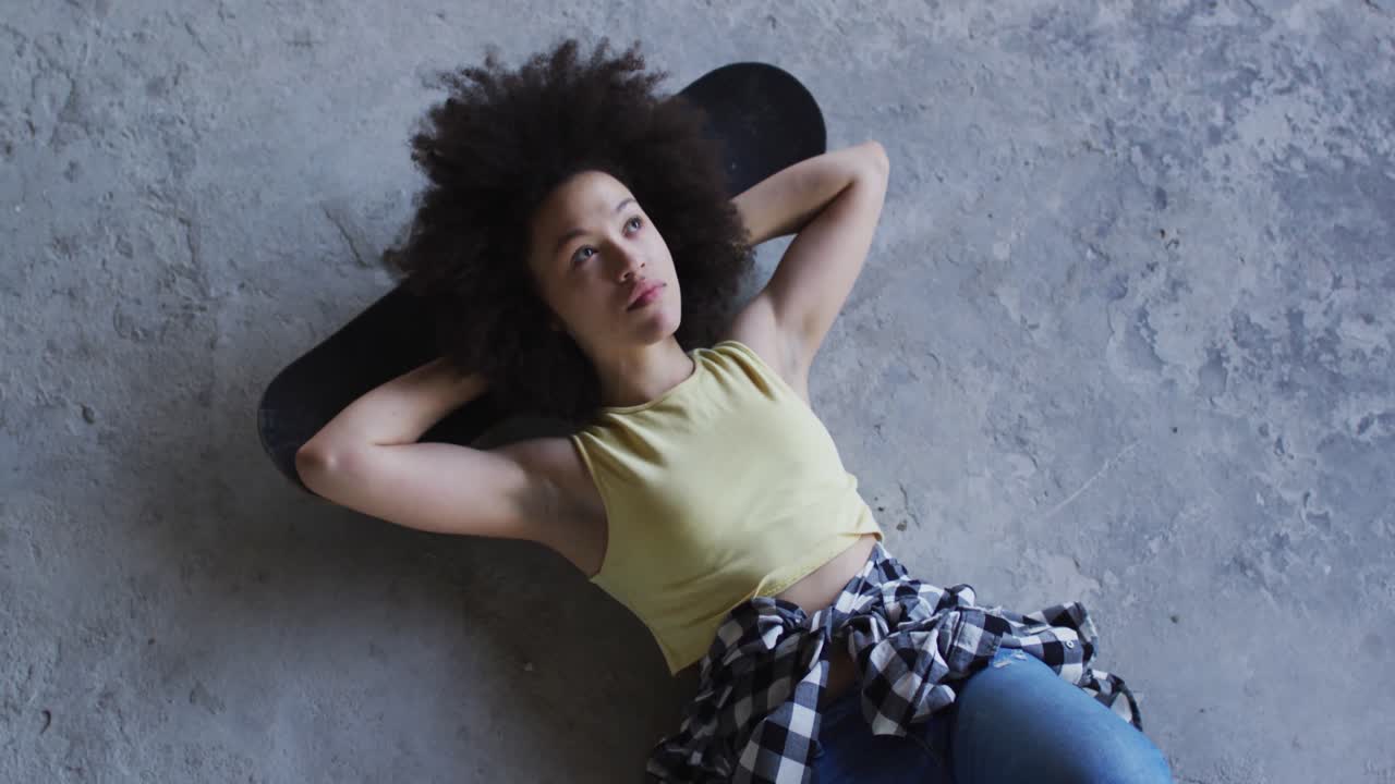 Mixed race woman in an empty building lying on a skateboard