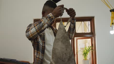 african american craftsman in checked shirt putting an apron on in leather workshop