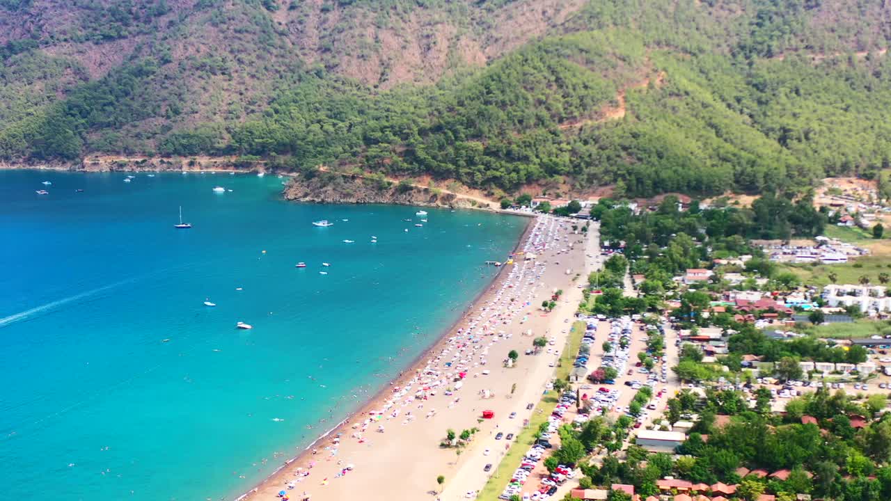 aerial view of Adrasan beach on a hot summer day in Turkey as people sun bathe while boats are anchored along the mountainous Mediterranean coastline