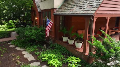 aerial shot of quaint american home displaying american flag above beautiful garden and landscaping foliage