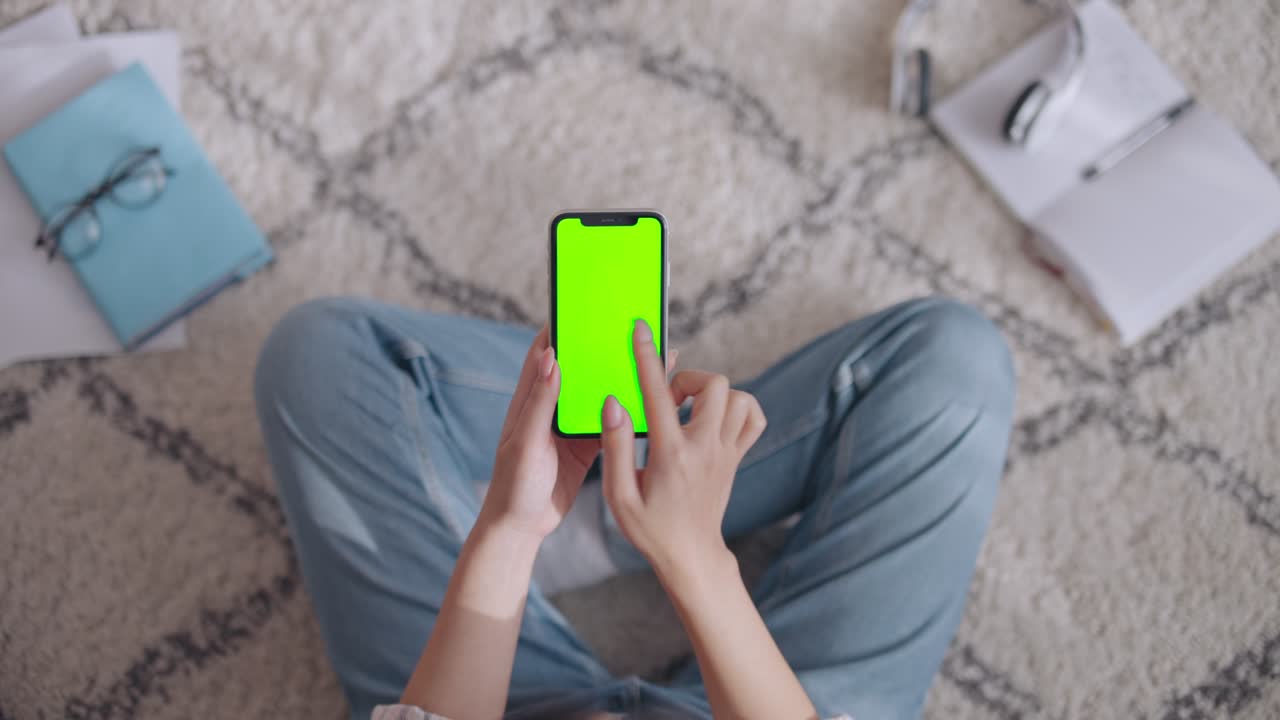 Woman scrolling, swiping and zooming on green screen smartphone, top view