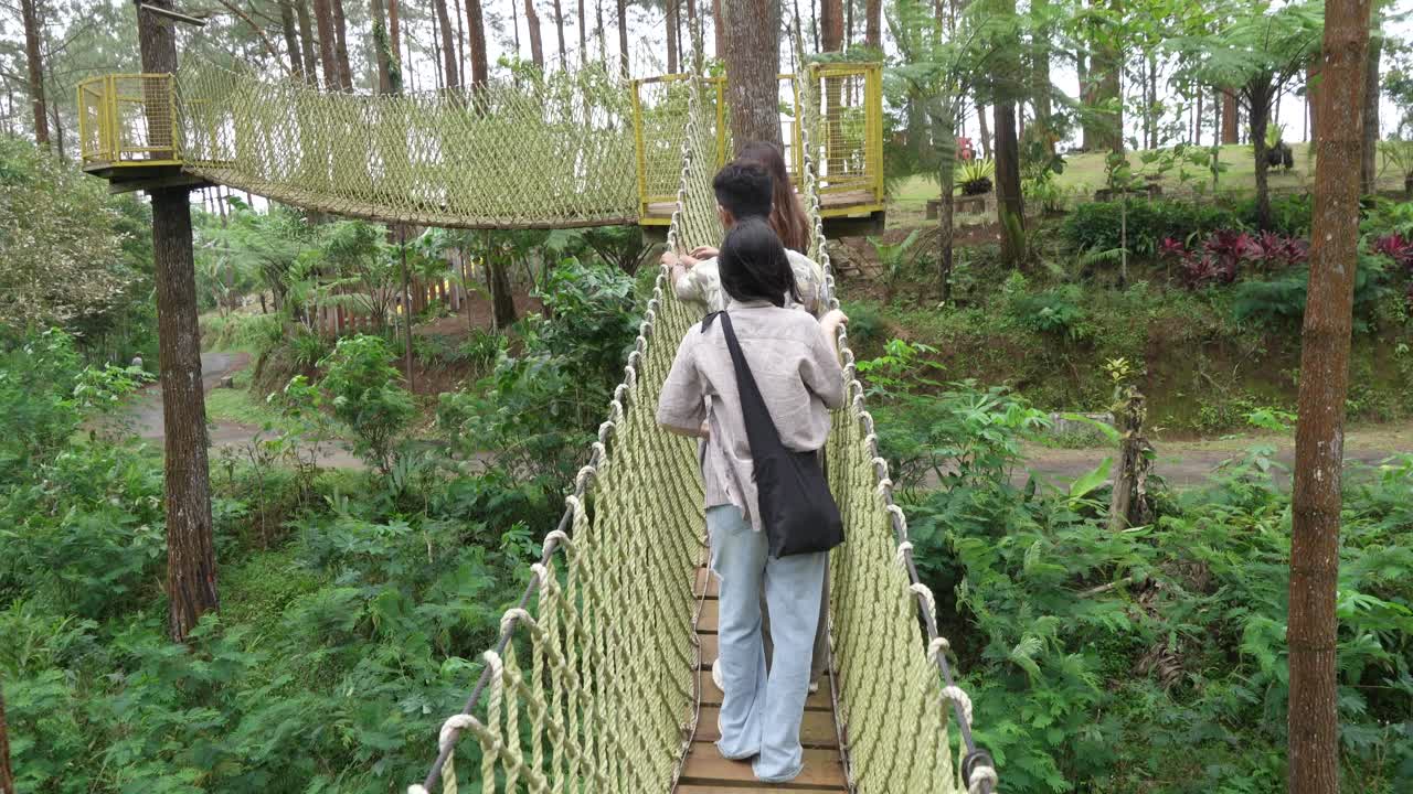 Young Asian Friends Crossing Rope Bridge in Forest Adventure