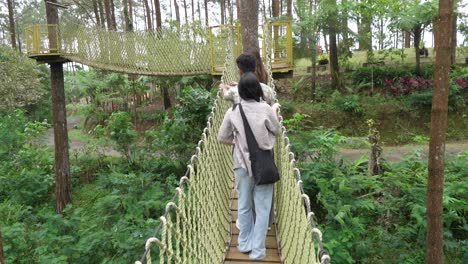 young asian friends crossing rope bridge in forest adventure