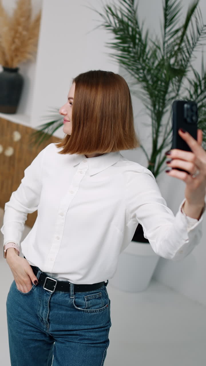 Bella giovane donna in camicia bianca che tiene in mano il telefono. La ragazza sta scattando un selfie e indica l'uomo seduto dietro. Ripresa dall'alto. Video verticale