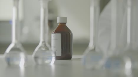 brown bottle with clear lab flasks on a white table in a laboratory