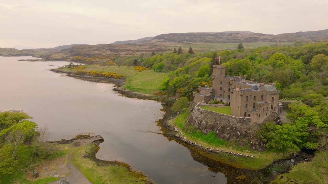 Aerial drone shot of Dunvegan Castle on the Isle of Skye, Scotland, with a scenic bay in the background, surrounded by lush greenery and rugged coastal beauty