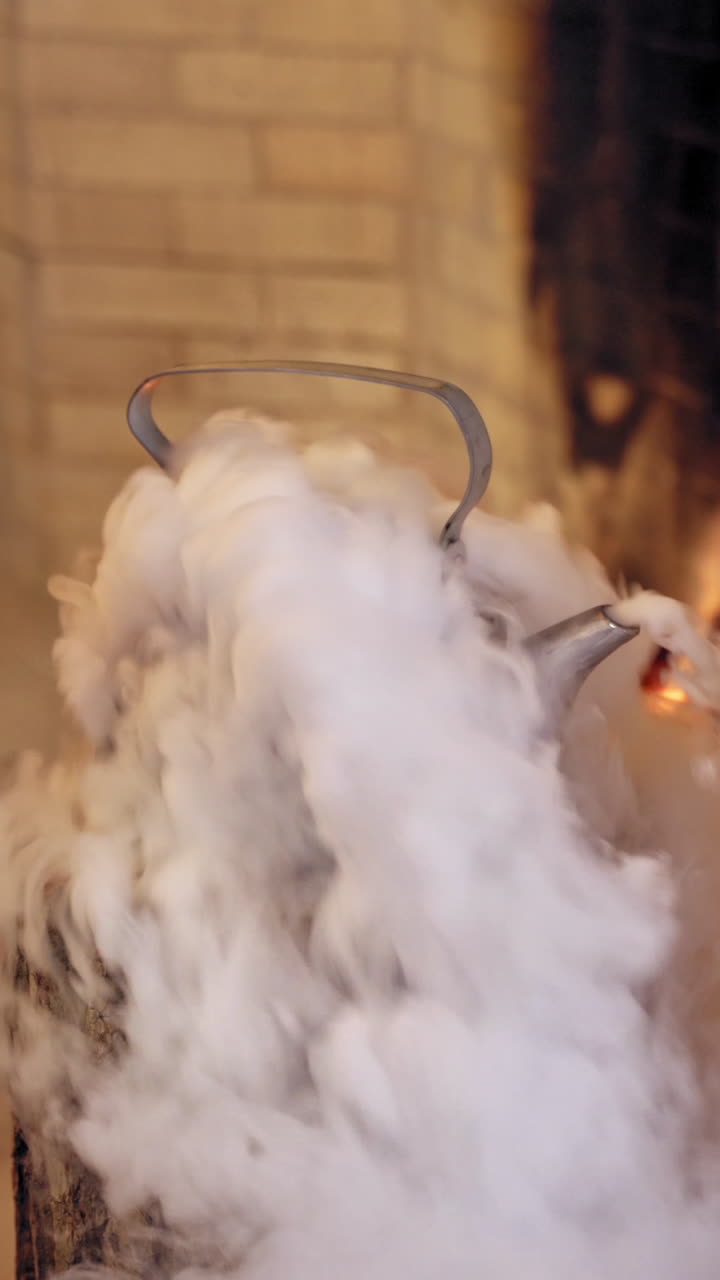 White steam coming from the kettle on a wooden log indoors. Boiling kettle near the fireplace. Santa's hand taking kettle with hot water. Vertical video
