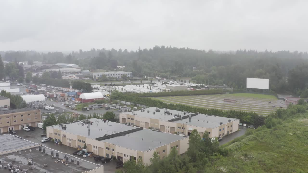 Aerial over commercial industrial building, drive-in theater over wet lands, green field, farms, marsh lands, and lots of rain on a summer day.