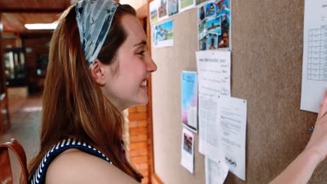 Smiling-schoolgirl-reading-notice-board-in-corridor