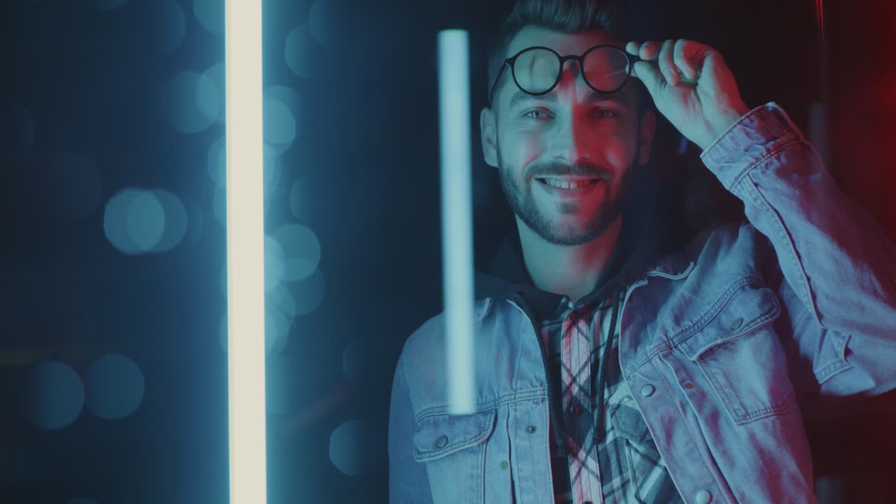 Man in Denim Jacket and Glasses Under Neon Lights
