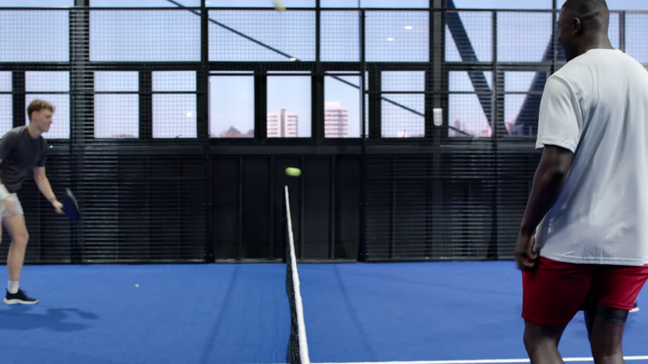 Two diverse men playing padel tennis on blue indoor court, focusing on intense match