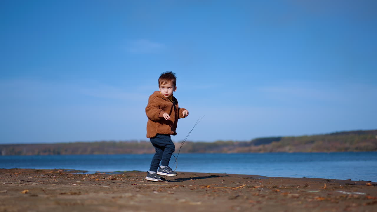 Lovely toddler boy walking to the river. Cute little kid throws the stone into water and walks away.