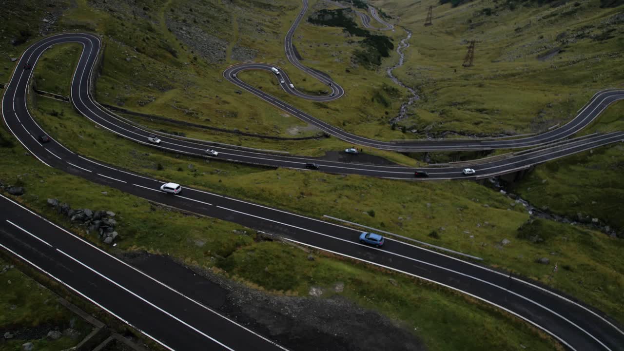 Dramatic drone reveal of Transfagarasan Road in Romania above thick clouds. Lush green mountain landscape and iconic winding highway in cinematic 4K.