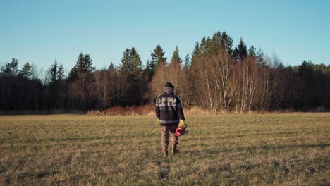 a man is going into the woods while carrying his chainsaw - static shot