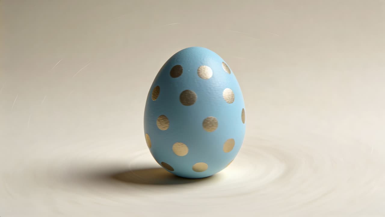 Rotating blue gold polka-dot egg shifting from soft camera tilt on beige tabletop, settling upright