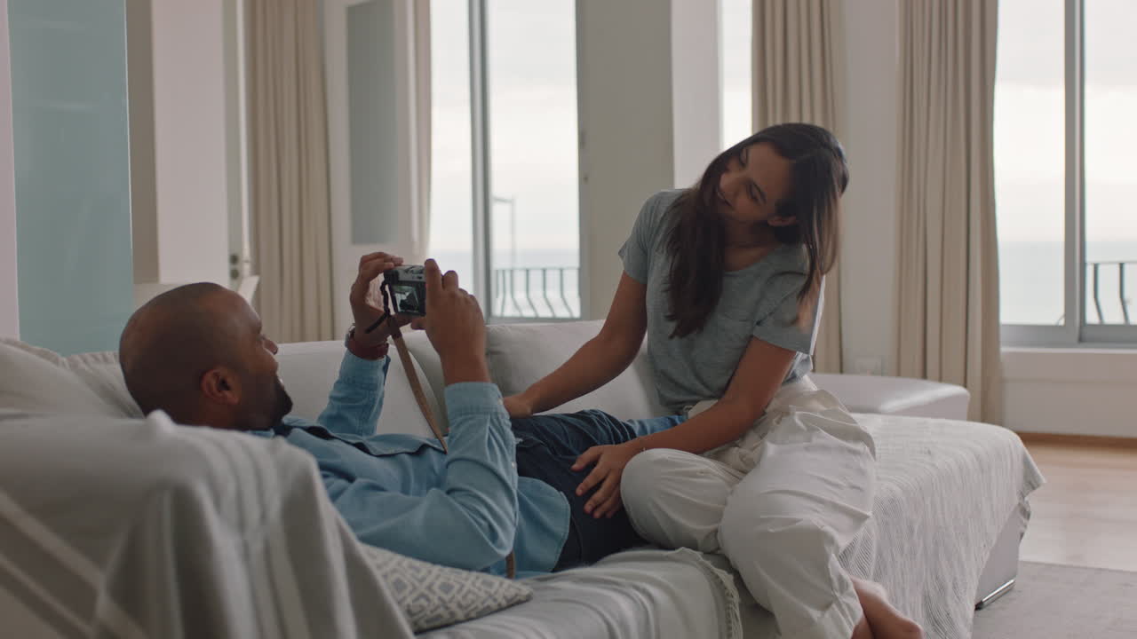 happy couple taking photos together using camera having fun relaxing at home on sofa enjoying romantic relationship playfully photographing each other