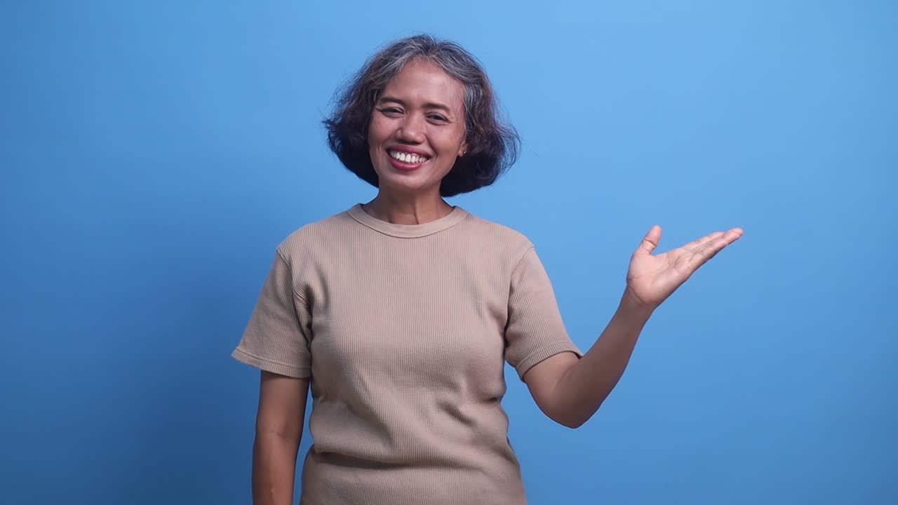 Middle age Asian woman smiling pointing to the side presenting over isolated blue background