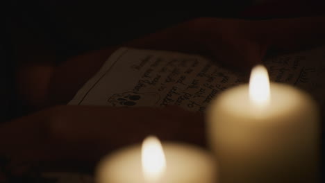hands of wiccan woman reading ancient pagan parchments in candlelight, medium shot