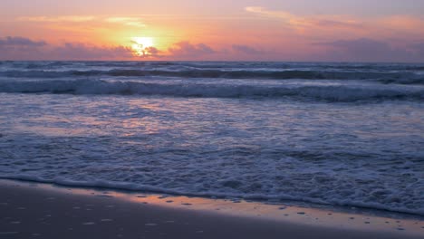 Beautiful-sunset-on-the-background-of-Baltic-sea,-sun-going-beyond-the-horizon-illuminating-water-and-clouds-in-the-sky,-calm-sea-waves,-romantic-mood,-copy-space,-low-medium-shot