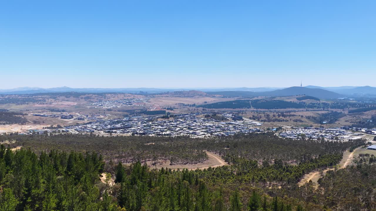 Powolne ujęcie panoramiczne przedstawia rozległe przedmieścia i odległe góry przy bezchmurnym niebie