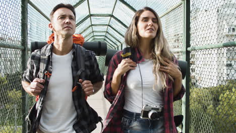 couple of travelers with backpacks walking on bridge from city