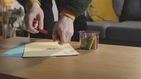 persona ordenando lápices de colores y papel en la mesa en casa para un niño diagnosticado con tea