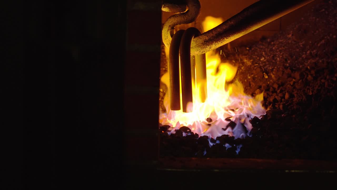 Close view of metal chain links heating in fire inside a blacksmith forge with glowing coals and intense flames
