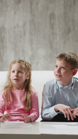 little blonde girl pupil answers nodding african-american tutor while brother classmate sits on sofa at home english lesson with native speaker slow motion