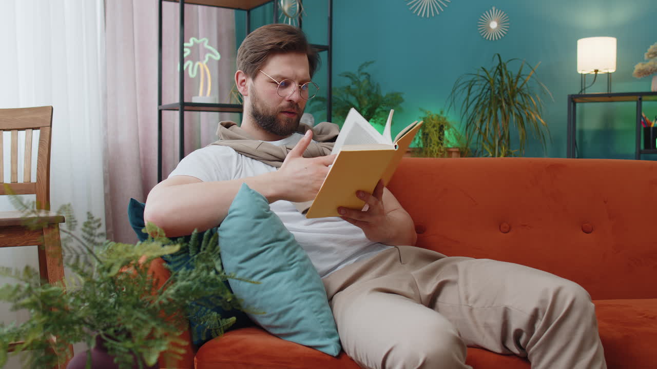 Jovem relaxando livro interessante virando páginas sorrindo desfrutando de literatura descansando no sofá