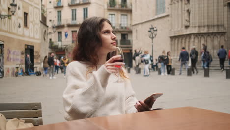 una joven sentada en un café bebiendo un vaso de vino tinto