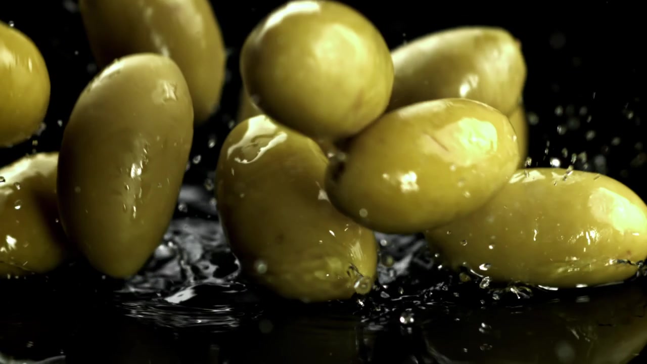 Olive verdi fresche che schizzano nell'acqua su sfondo nero
