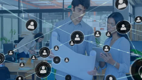 office team collaborating over blueprints and tablet in tech office, showing network icon overlays