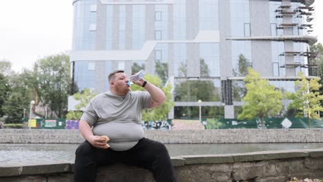 portrait of an overweight man sitting outside eating a bun and drinking water portrait of an overweight man sitting outside eating a bun and drinking water a fat man on the background of a building in the city