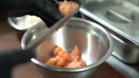 Chef-hands-with-black-gloves-pours-salmon-cubes-into-a-steel-container