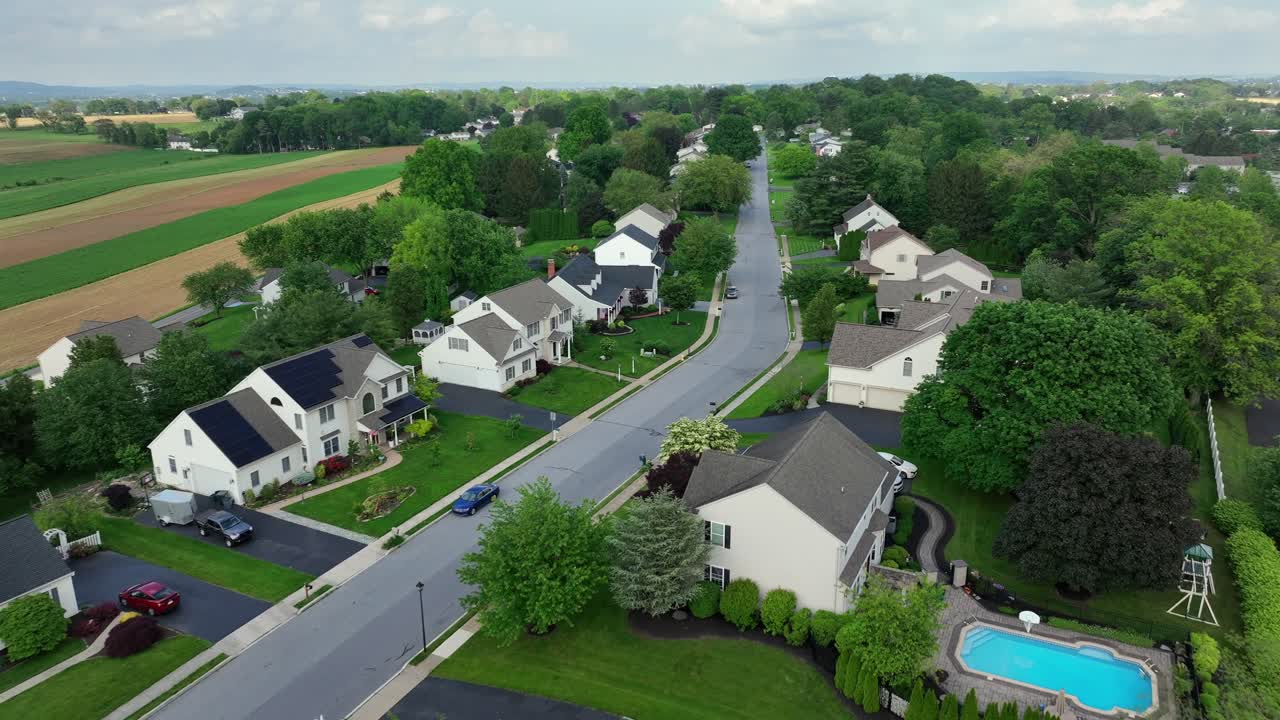 Luxury one family houses with solar panels on roof with swimming pool in yard. Aerial forward wide shot. Cloudy and rainy day in America. Rural farm fields in distance in May. No production of energy.