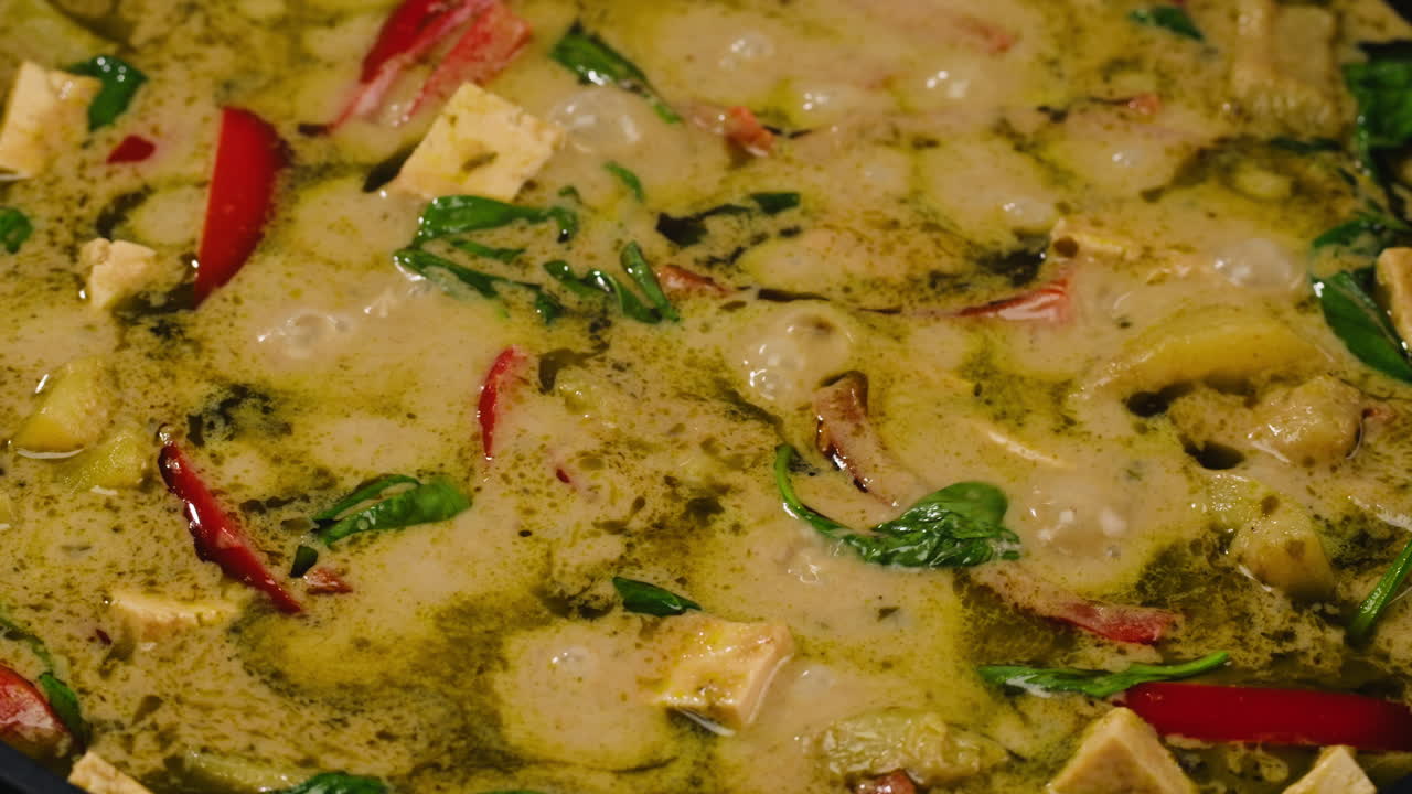 Close-up of simmering green curry with tofu and chili peppers