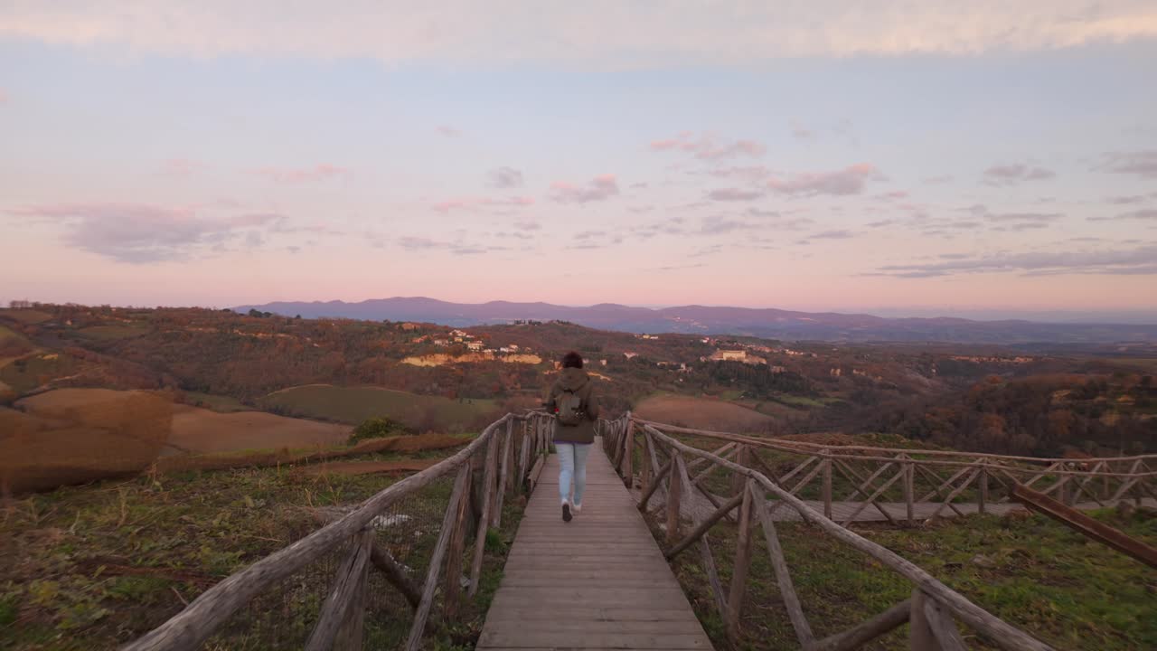 Woman jogs on boardwalk trail towards scenic sunset view of Celleno, Italy hills