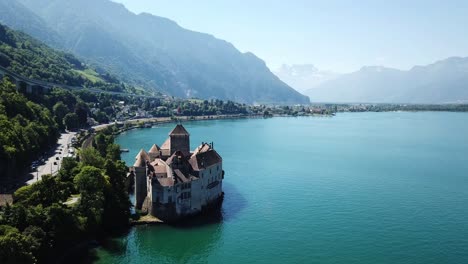 aerial view of château de chillon, an ancient castle on lake geneva's edge, surrounded by turquoise water and backed by the swiss alps on a clear day, capturing the serene beauty of the landscape