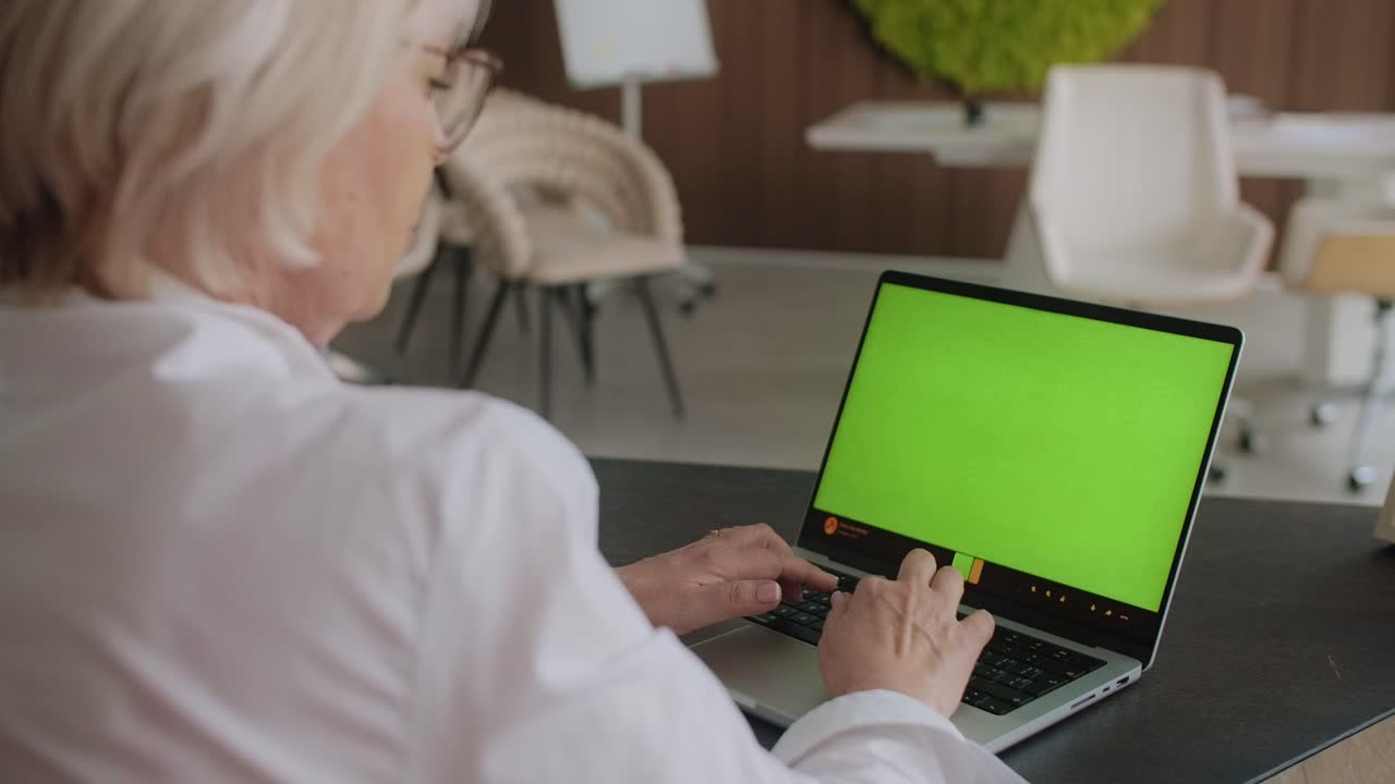 mujer mayor trabajando en una computadora portátil en una oficina moderna
