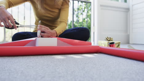 midsection of biracial woman sitting on floor packing christmas presents, slow motion