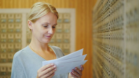 Attraktive-Frau-Sieht-Briefe-Im-Postamt-Auf-Dem-Hintergrund-Von-Briefkästen-Durch