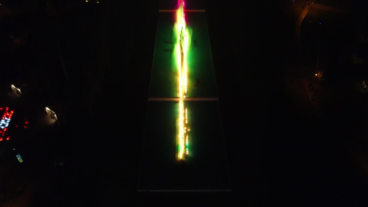 Night time drone video of a water park with colorful fountains