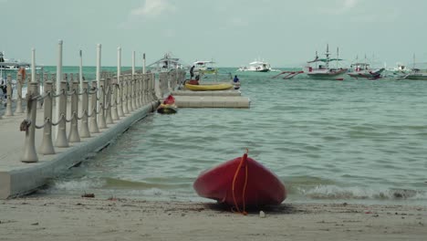 el nido, philippines - red boat docked on the sandy shore on a sunny day with boats adrift on the sea in the background - closeup shot