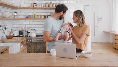 familia ocupada en la cocina en el desayuno con la madre trabajando en la computadora portátil y el padre cuidando al hijo bebé