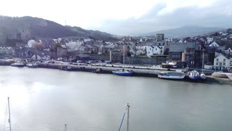 Idyllisches-Conwy-Castle-Und-Hafenfischerstadtbild-An-Der-Küste-Am-Wasser,-Antenne,-Die-über-Boote-Unten-Umkehrt